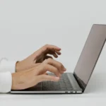 Close-up of hands typing on a laptop keyboard checking written text