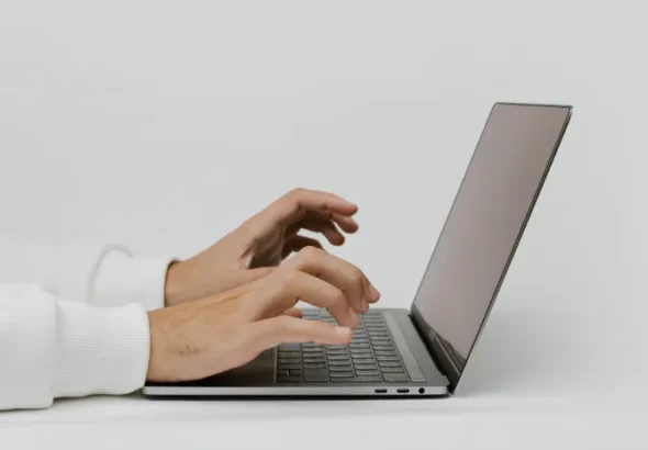 Close-up of hands typing on a laptop keyboard checking written text